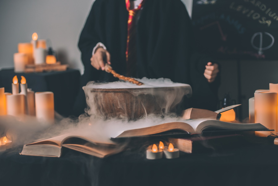 Photo of a cauldron with a person pointing a want to it, mist coming out of the cauldron