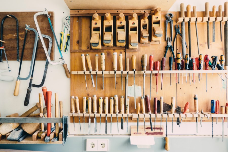 Photo of all sort of tools hanging on a wall, like hammers, saws, etc.
